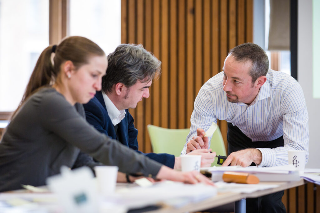 Two people working at a table while a trainer speaks to them